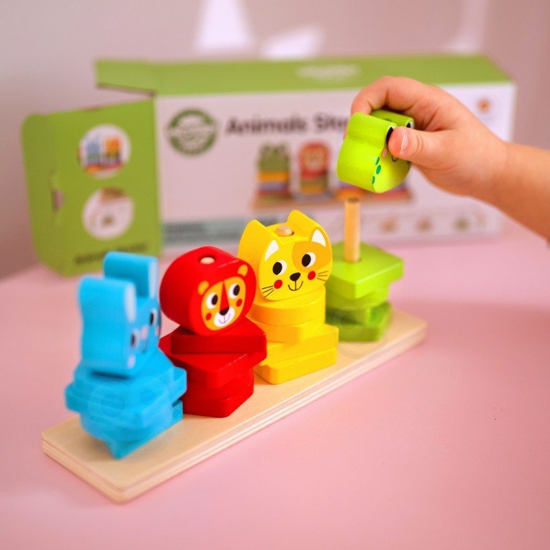 1. Child's hand placing green animal block on Montessori puzzle pyramid with colorful animal shapes on pink table