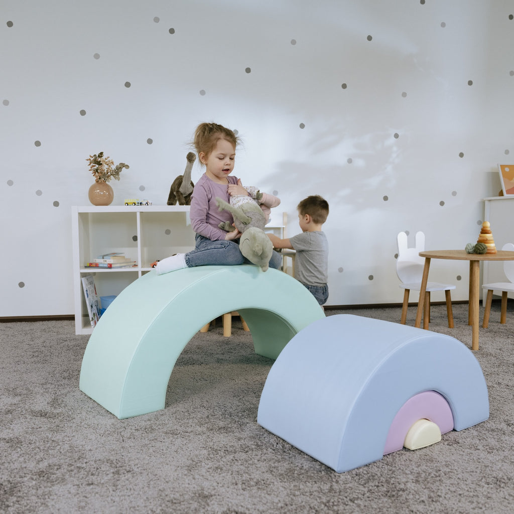 10. Girl sitting on pastel rainbow soft play set with boy playing in background
