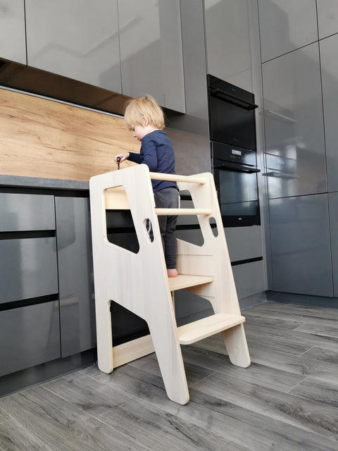 1. Child using natural birch Montessori Tower Safety+ at kitchen counter, demonstrating its practical use and safety features