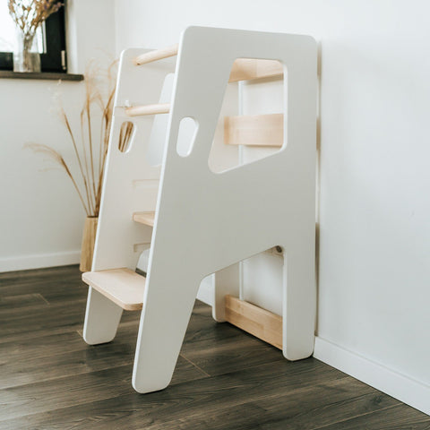 1. Montessori Tower Safety+ in white finish against a white wall with wooden floor, showcasing its ergonomic design and adjustable platform