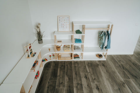 1. Overhead view of Montessori modular shelving and wardrobe system in white and natural wood, arranged in a corner on dark wooden flooring