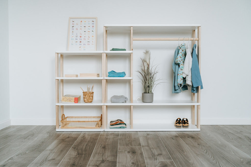 2. Montessori wardrobe with white shelves and natural wood accents, displaying children's clothing and decor, set against a white wall