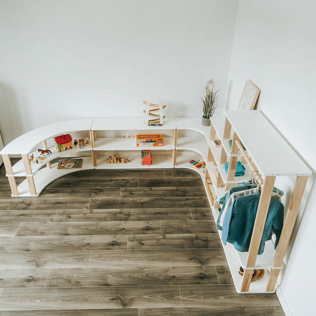 1. Top view of Montessori modular shelving and wardrobe system in white and natural wood, arranged in a corner on dark wooden flooring