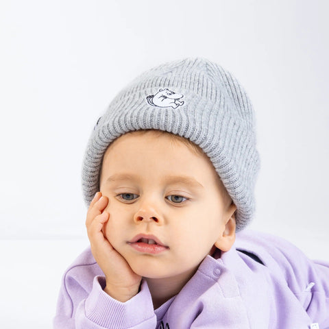 1. Child wearing grey Moomintroll beanie with felt patch, resting head on hand, in a studio setting