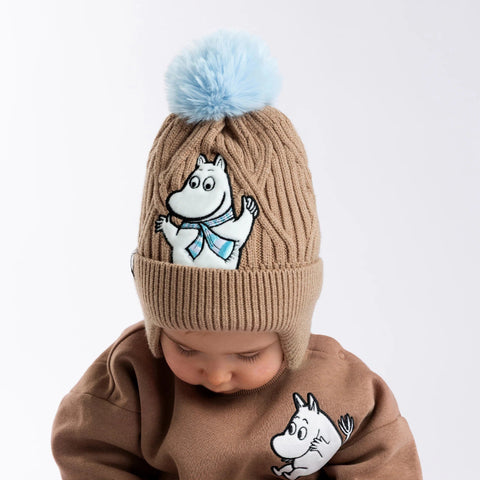 1. Child wearing brown Moomintroll winter beanie with blue pom-pom and fleece lining, featuring Moomintroll character, in studio setting