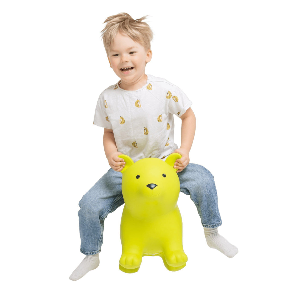 1. Child wearing white shirt with yellow print and jeans sitting on green bear-shaped hopper toy indoors
