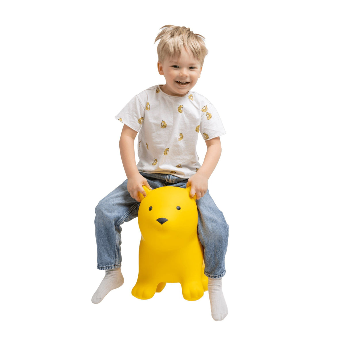 1. Child wearing white shirt with yellow print and jeans sitting on yellow bear-shaped hopper toy indoors