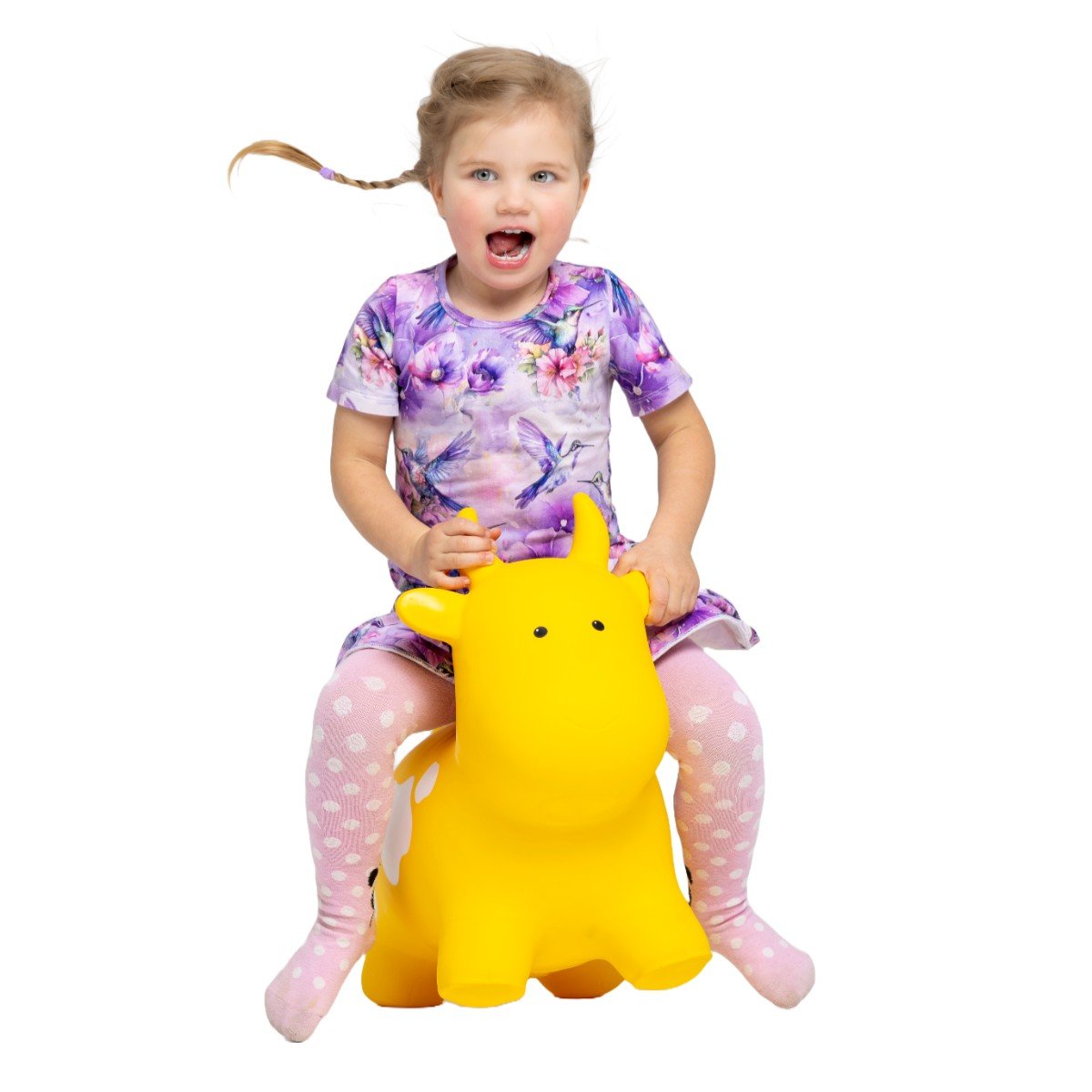 1. Young girl in a purple floral dress and pink polka dot tights sitting on a yellow cow-shaped hopper toy by Gerardo's Toys, smiling with excitement