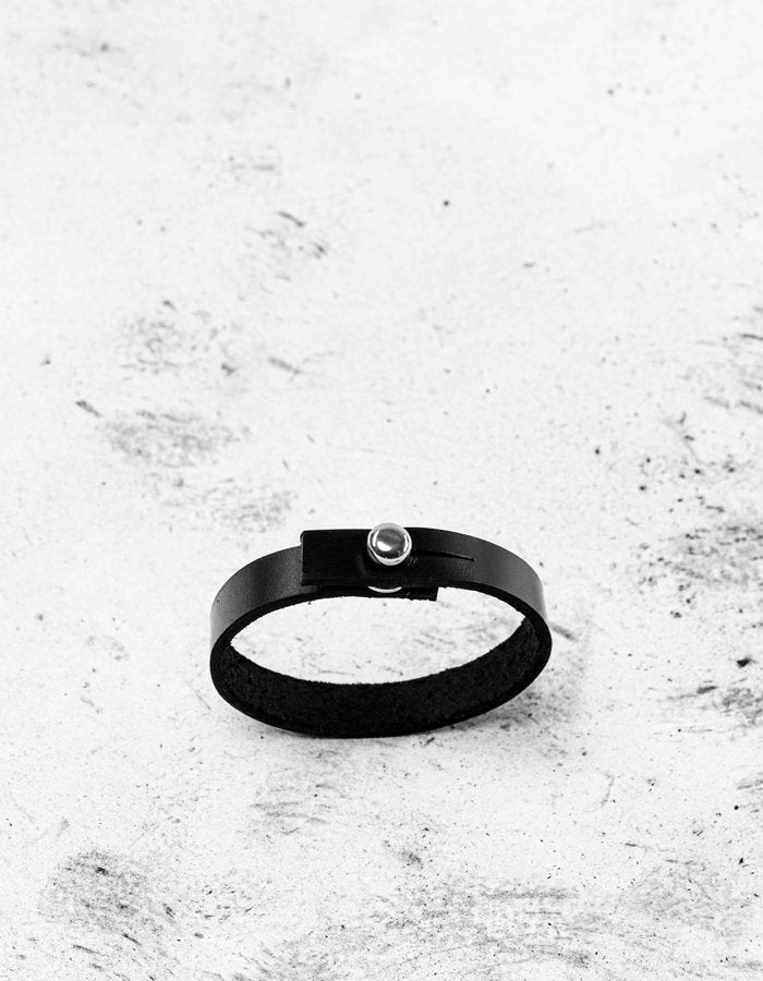 3. Close-up of black leather wristband with silver screw button on textured surface