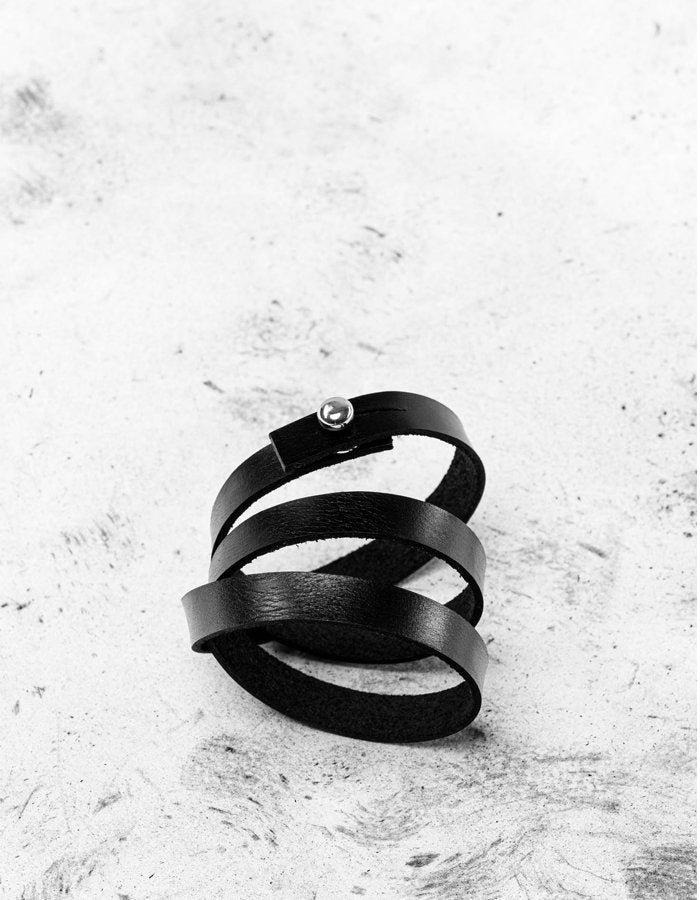 3. Close-up of black leather wristband with screw button on textured surface