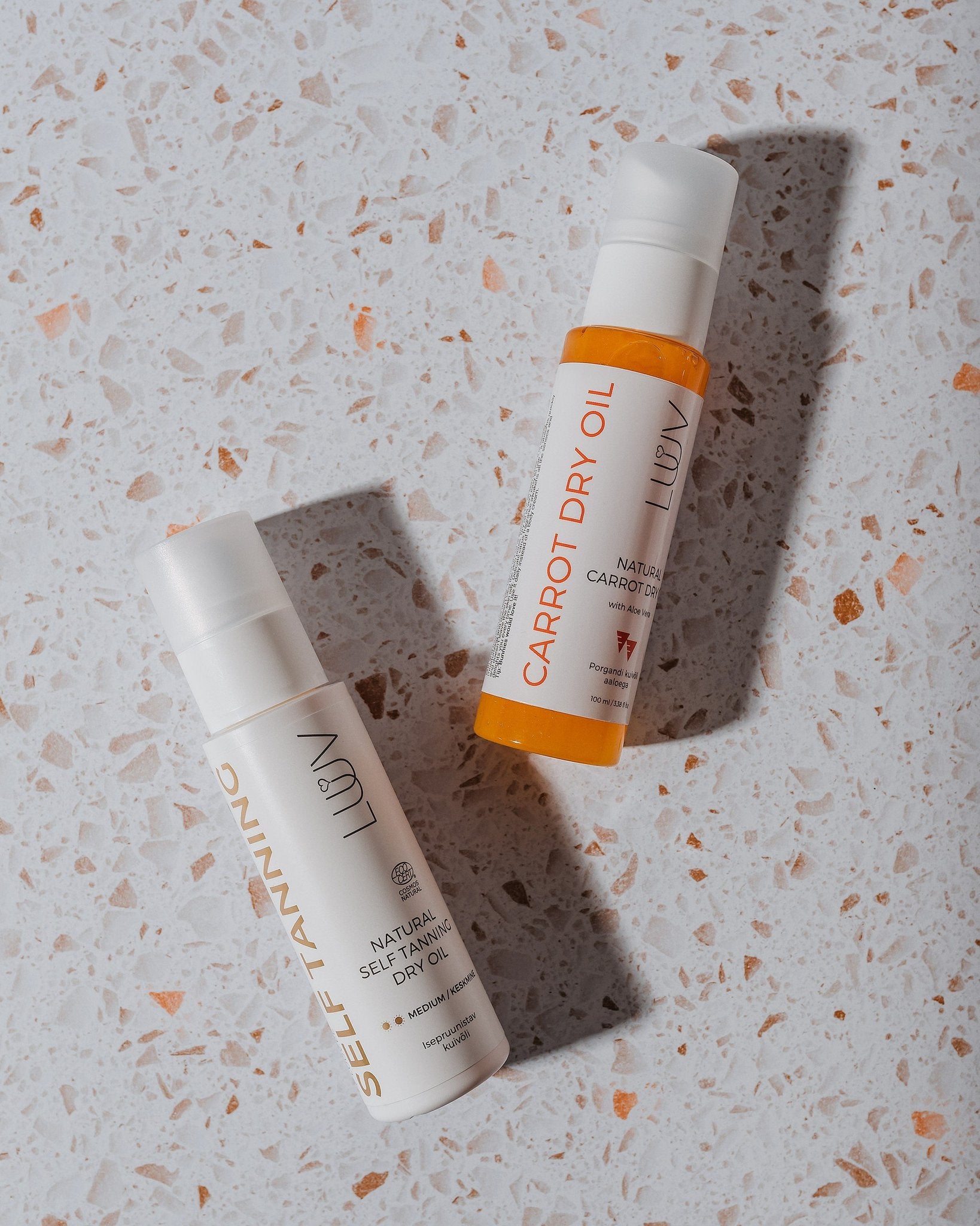 5. Flat lay of LUUV Carrot Dry Oil and Self-Tanning Oil on a speckled surface