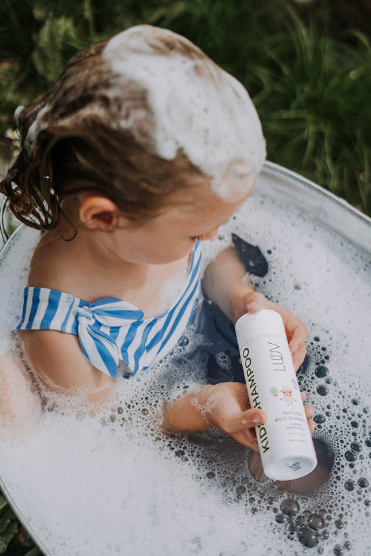 1. Child in striped swimsuit using LUUV Natural Kid's Shampoo Pear COSMOS in outdoor bath setting
