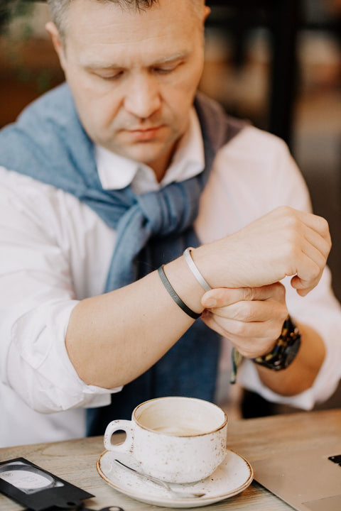 1. Man wearing silver and black bracelets, sitting at a table with a coffee cup, adjusting wristwear