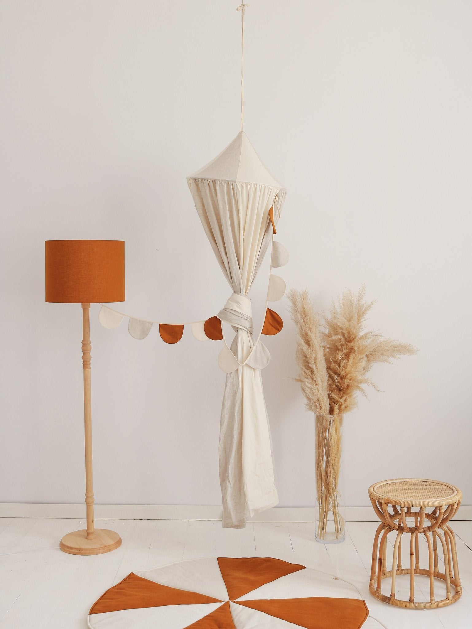 2. Cream canopy tied with garland next to orange lamp and wicker stool in a cozy room