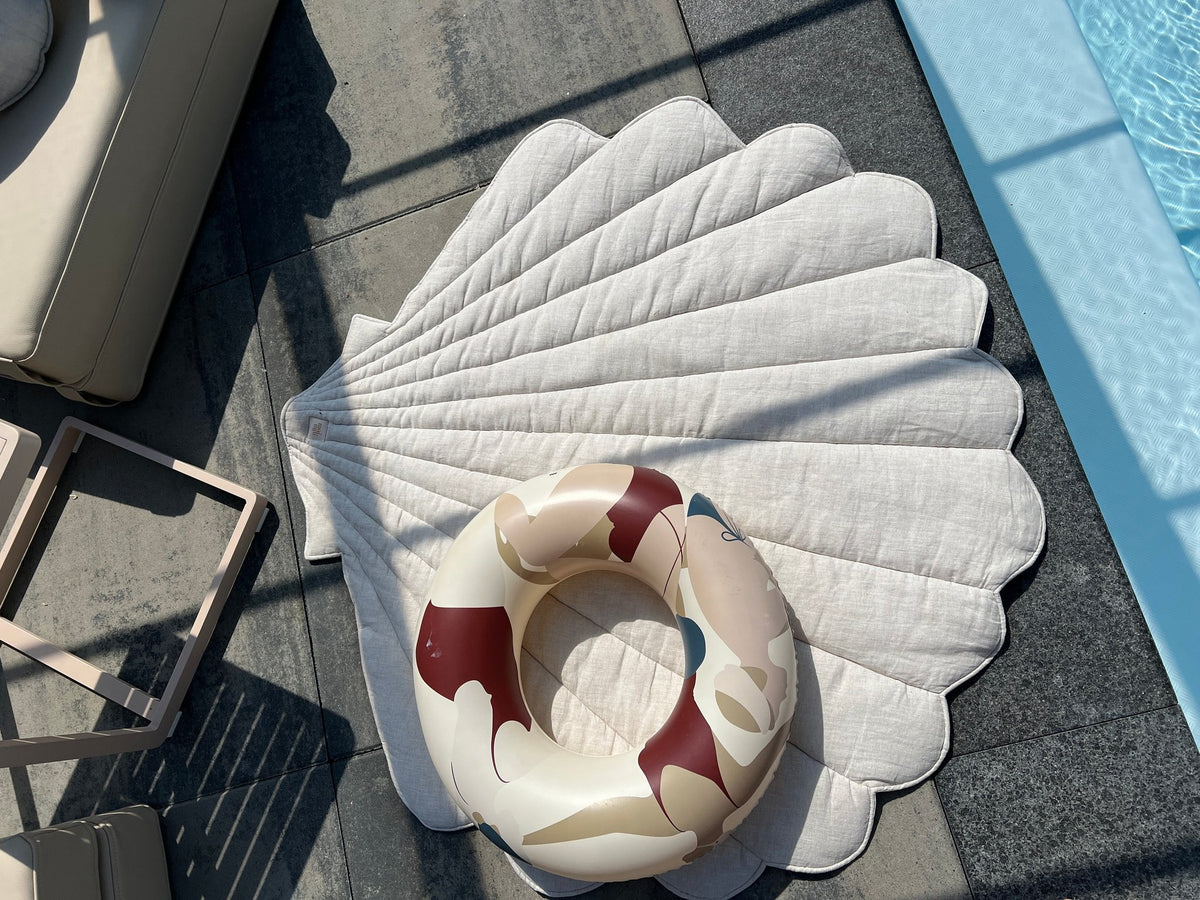 1. Organic cotton and linen shell playmat in sand color by a poolside with a colorful inflatable ring