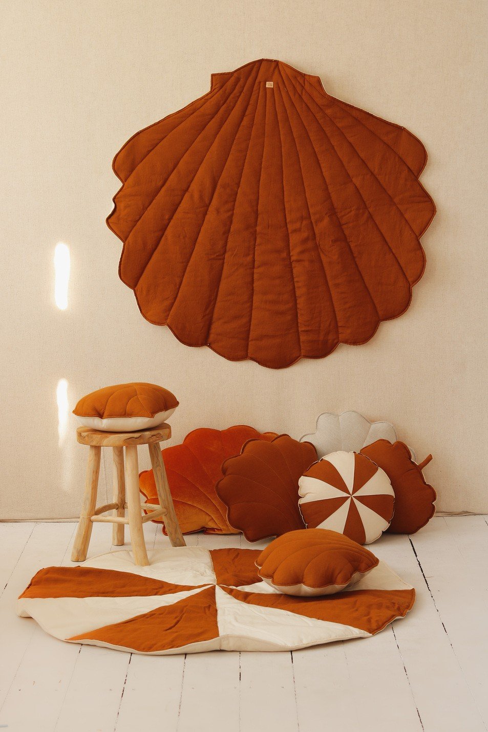 4. Flat lay of caramel shell playmat with matching cushions and a wooden stool on a white wooden floor