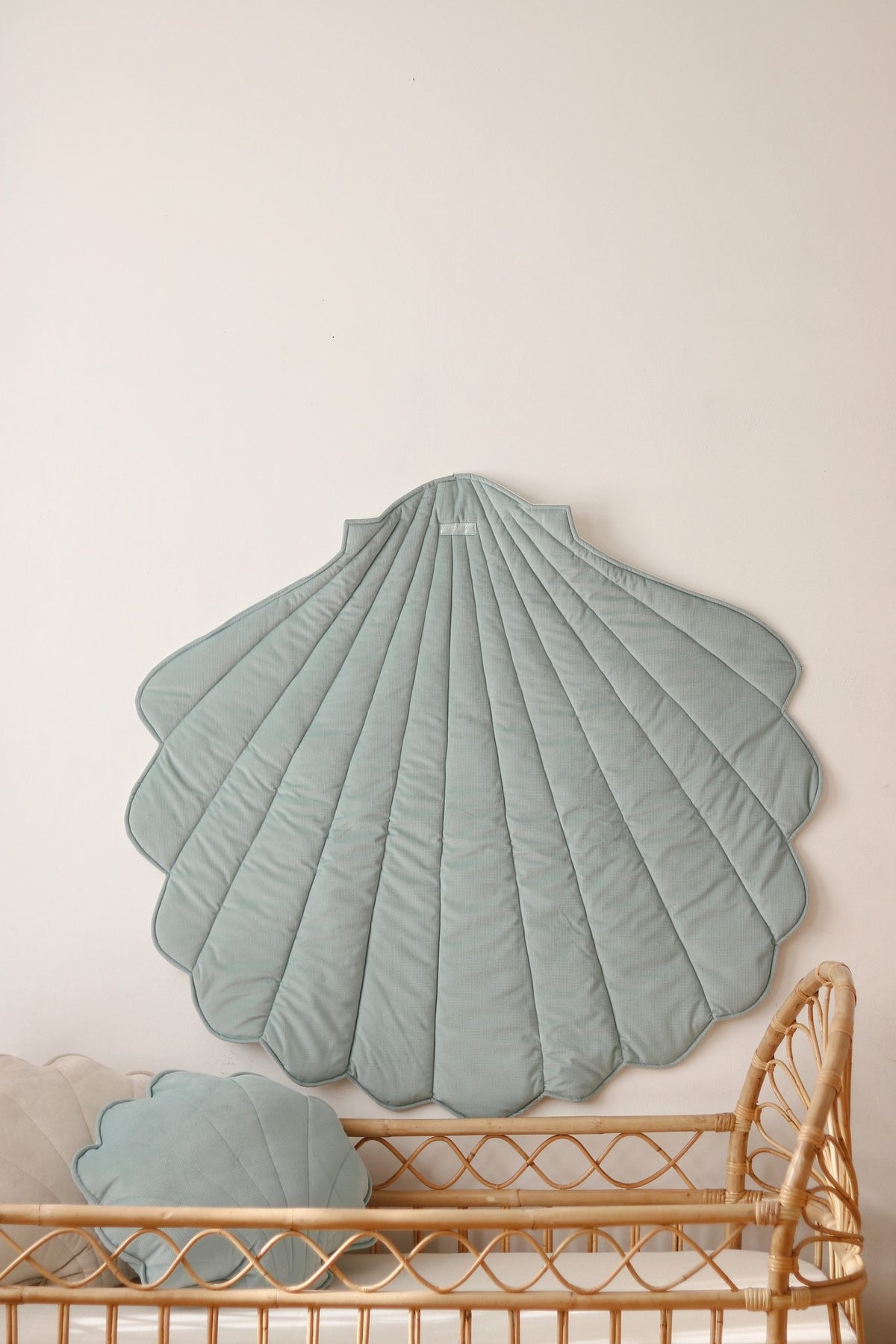 1. Mint green shell-shaped playmat hanging on wall above wicker crib in nursery setting