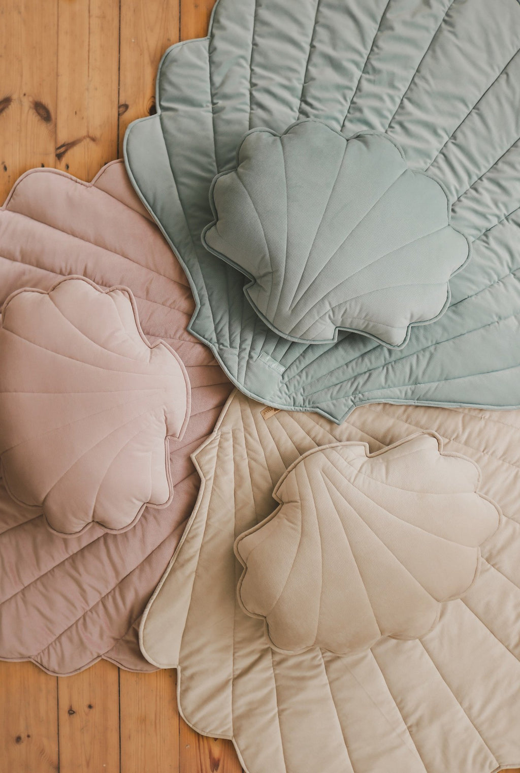 4. Flat lay of shell-shaped playmats in mint, pink, and beige with matching pillows on wooden floor