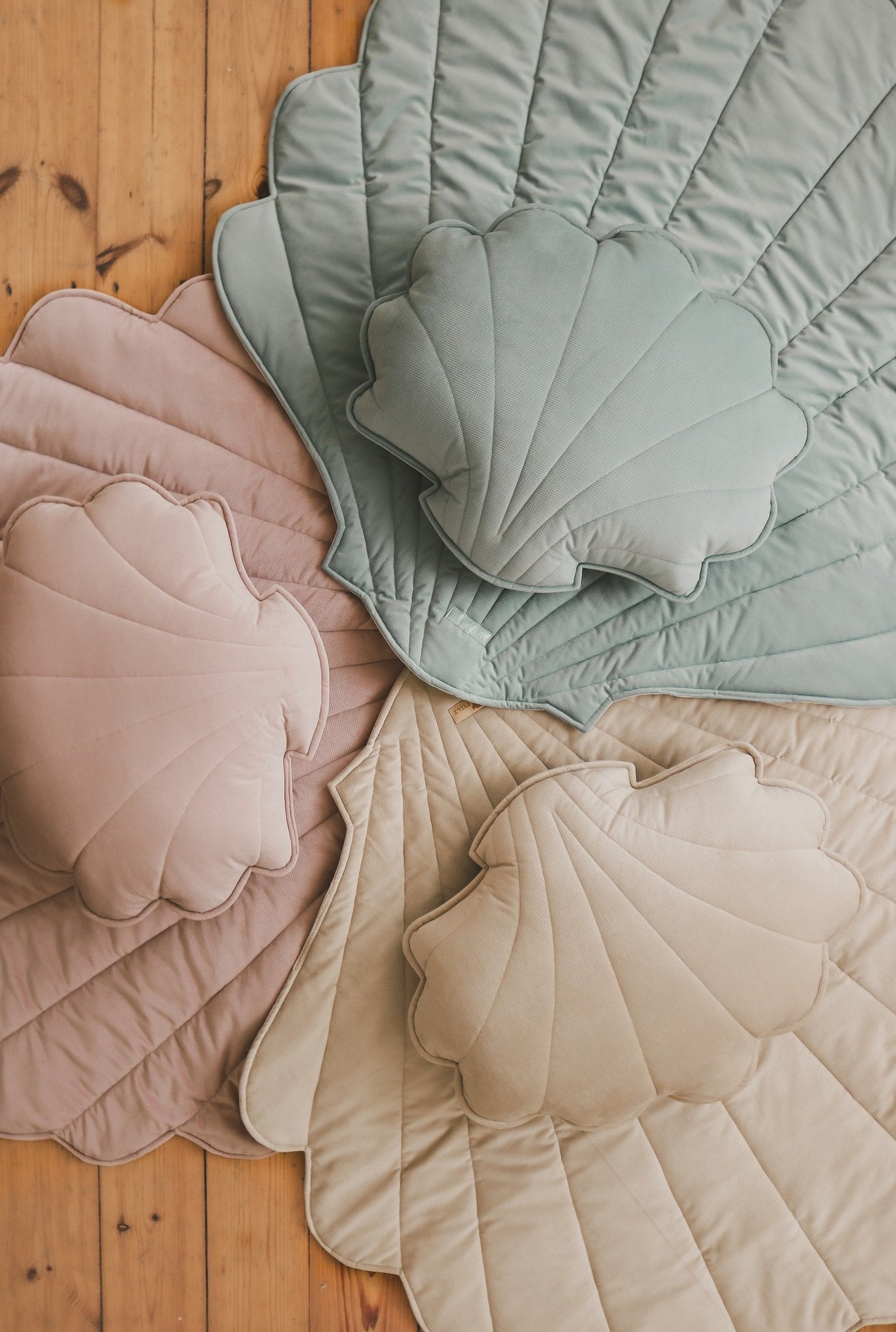 4. Flat lay of shell-shaped playmats in mint, pink, and beige with matching pillows on wooden floor