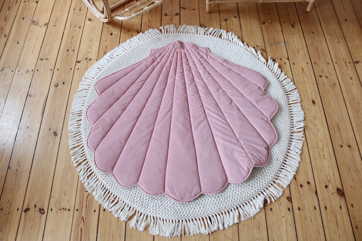 1. Powder pink shell-shaped playmat on a round woven rug on wooden floor