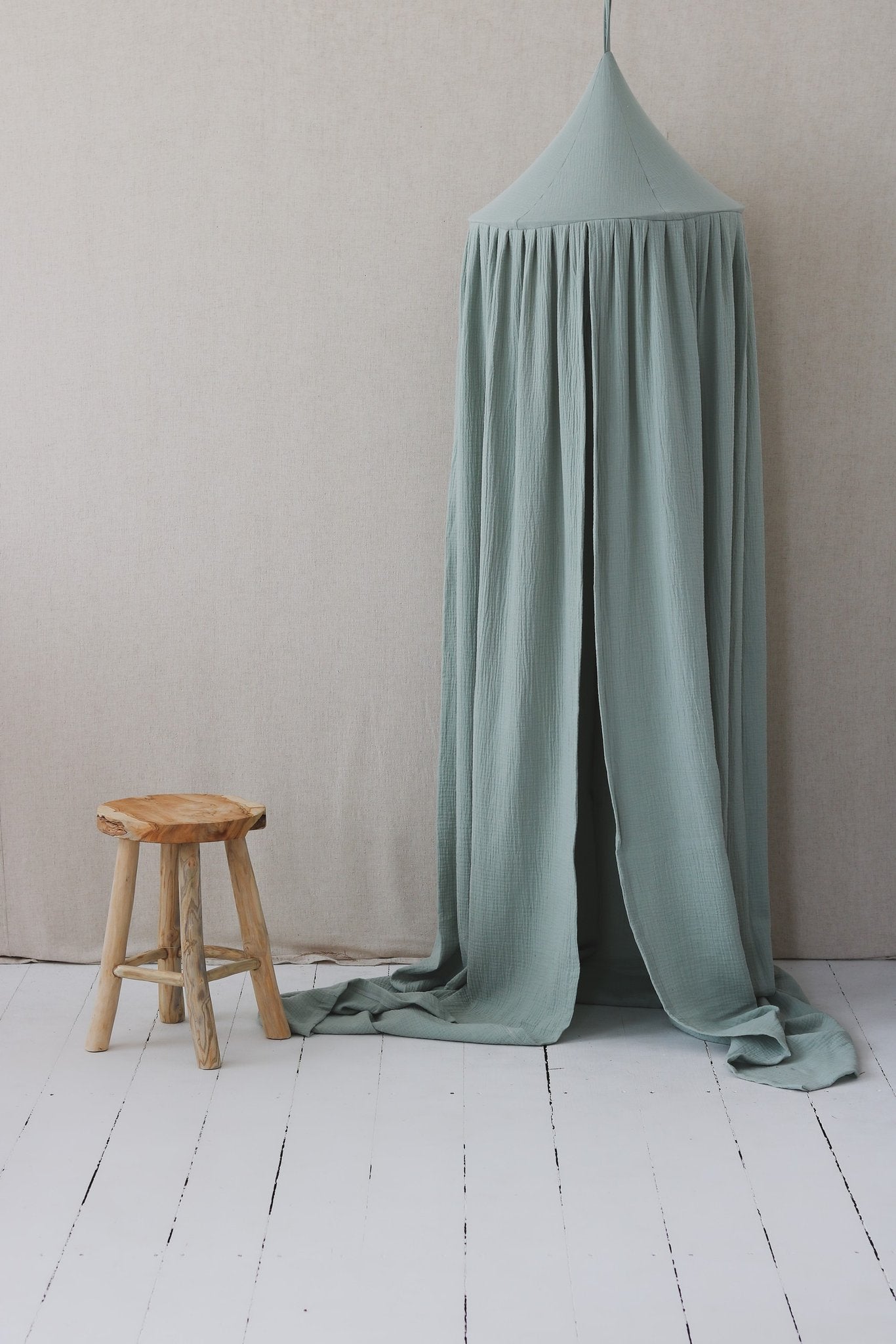 3. Mint green cotton canopy next to a wooden stool in a minimalist room