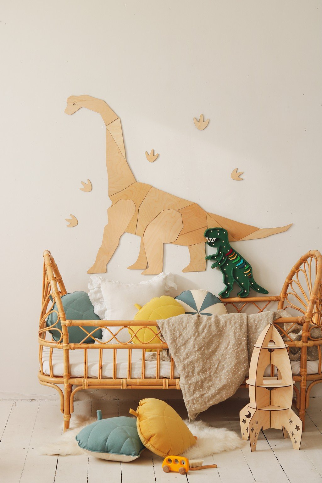 6. Wooden diplodocus wall decoration above rattan crib with colorful pillows and dinosaur footprints