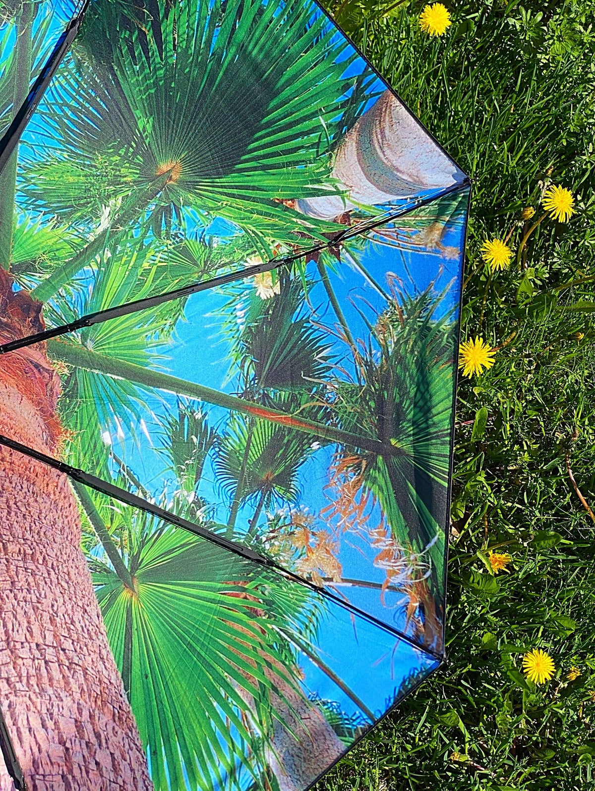 9. Paradise Umbrella with tropical print open on grass, surrounded by yellow flowers