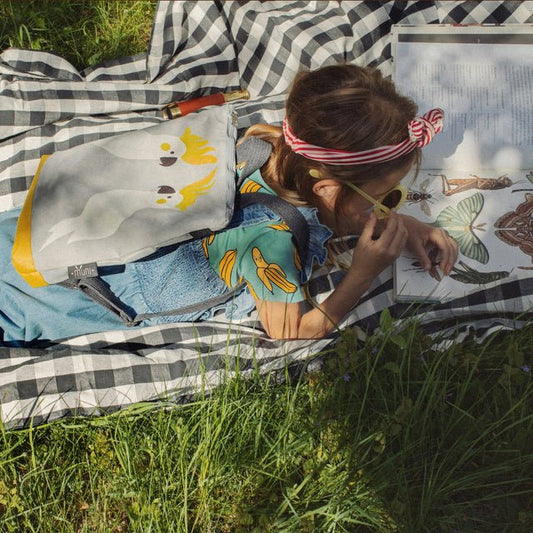 2. Girl lying on grass with Muni Cockatoo kids backpack, highlighting outdoor adventure