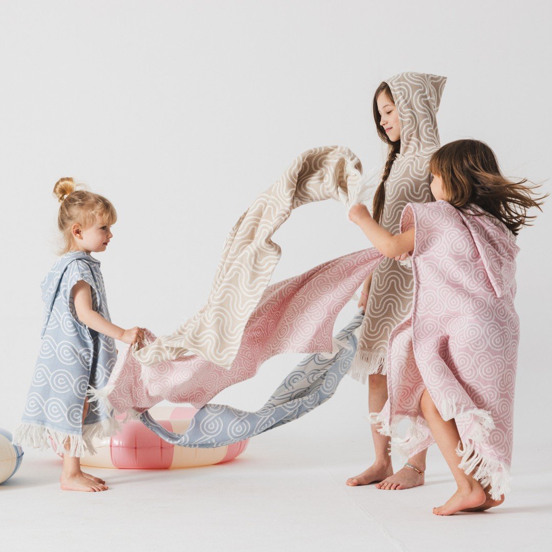 1. Three children playing with Patulove bamboo towels in pink, beige, and blue with hoods in a playful setting