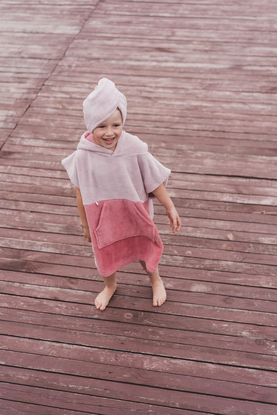 5. Child in pink bath poncho and hair turban standing on wooden deck