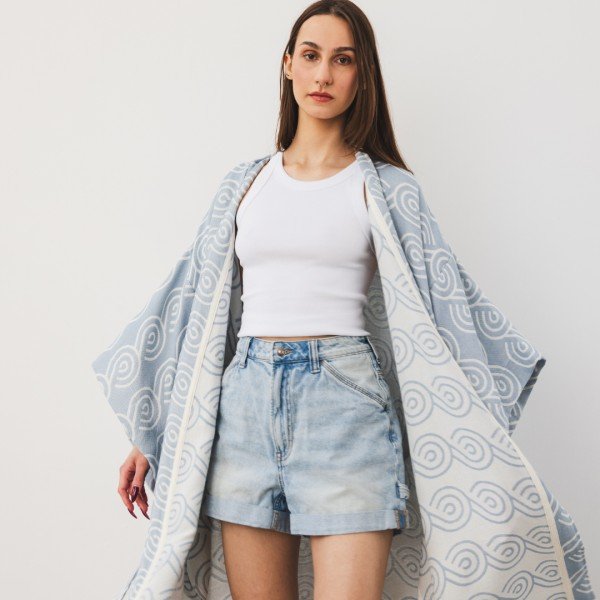 1. Woman wearing Patulove blue bamboo kimono over white top and denim shorts in studio setting