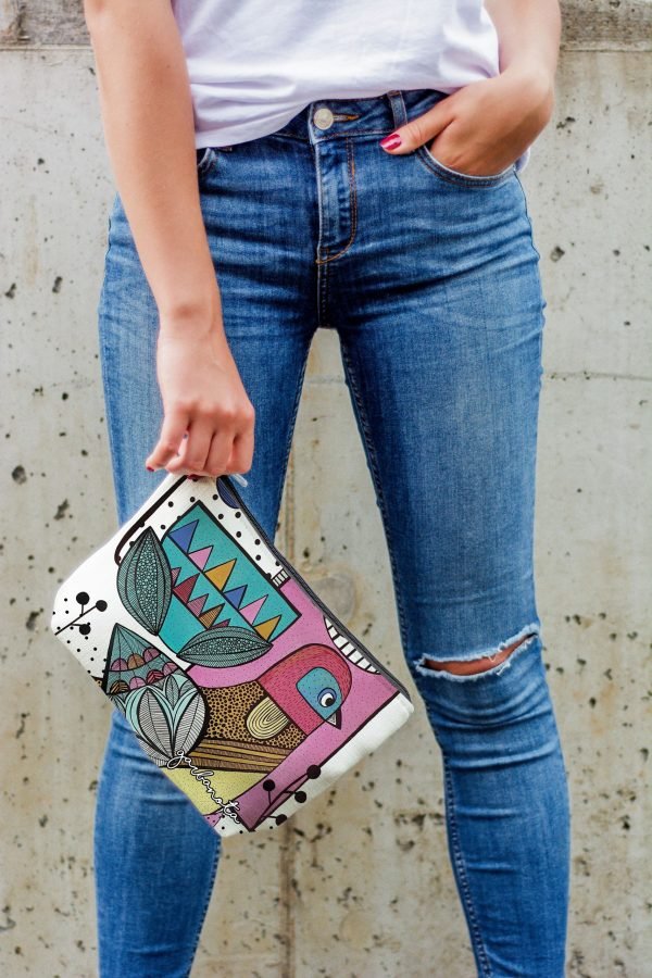 3. Woman standing against wall holding Garbanota Little Bird makeup bag, emphasizing unique artistic print and casual outfit