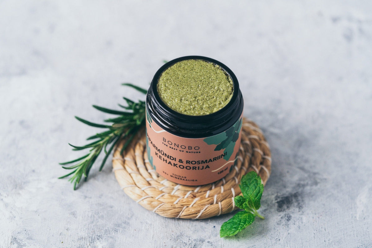 3. Open jar of BONOBO Peppermint & Rosemary body scrub on a woven mat with rosemary and mint leaves