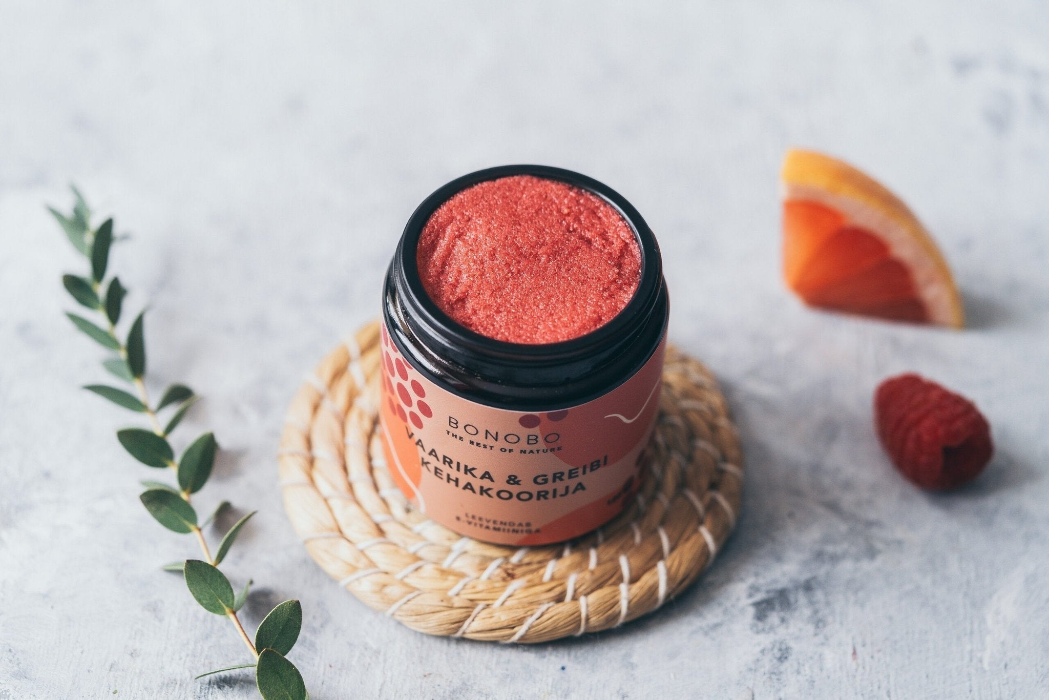 3. Open jar of BONOBO Raspberry & Grapefruit body scrub on a woven mat with raspberry and grapefruit slice