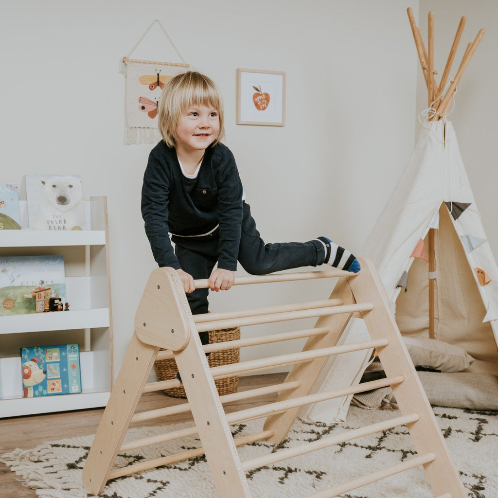 2. Child in black outfit climbing natural wood Pikler Triangle in playroom with teepee