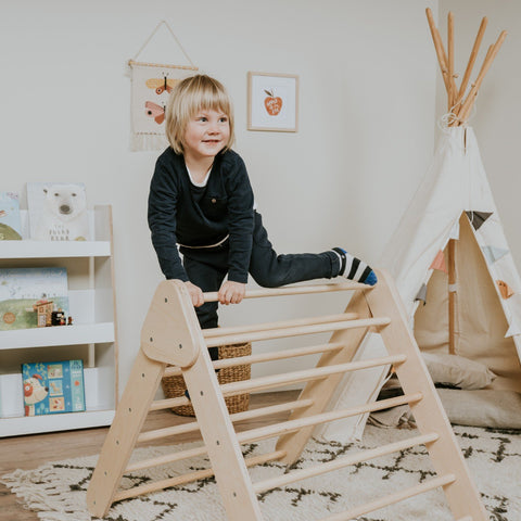 2. Child in black outfit climbing natural wood Pikler Triangle in playroom with teepee