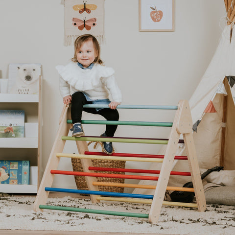 1. Child sitting on leg&go Pikler Triangle with rainbow bars in cozy playroom setting