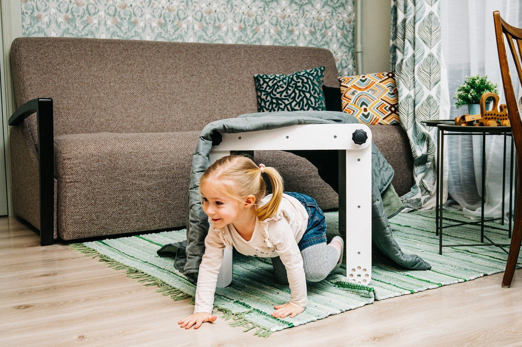 6. Girl crawling under a white Pikler triangle covered with a blanket in a living room