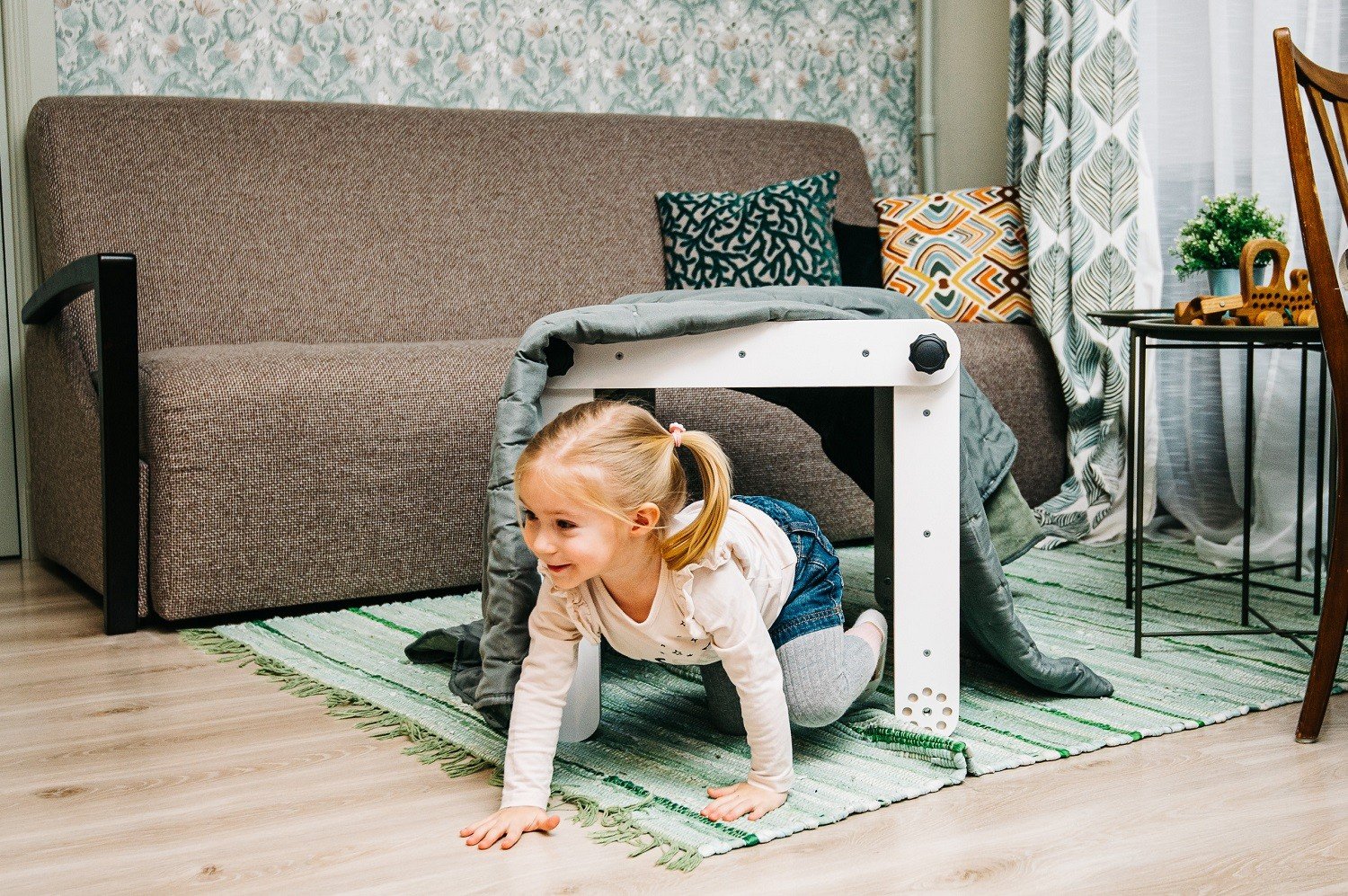 6. Girl crawling under a white Pikler triangle covered with a blanket in a living room