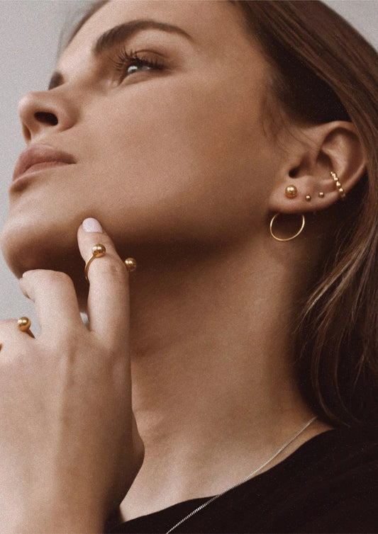 2. Women's gold pin-up earrings worn by model with additional gold jewelry, shown in lifestyle setting