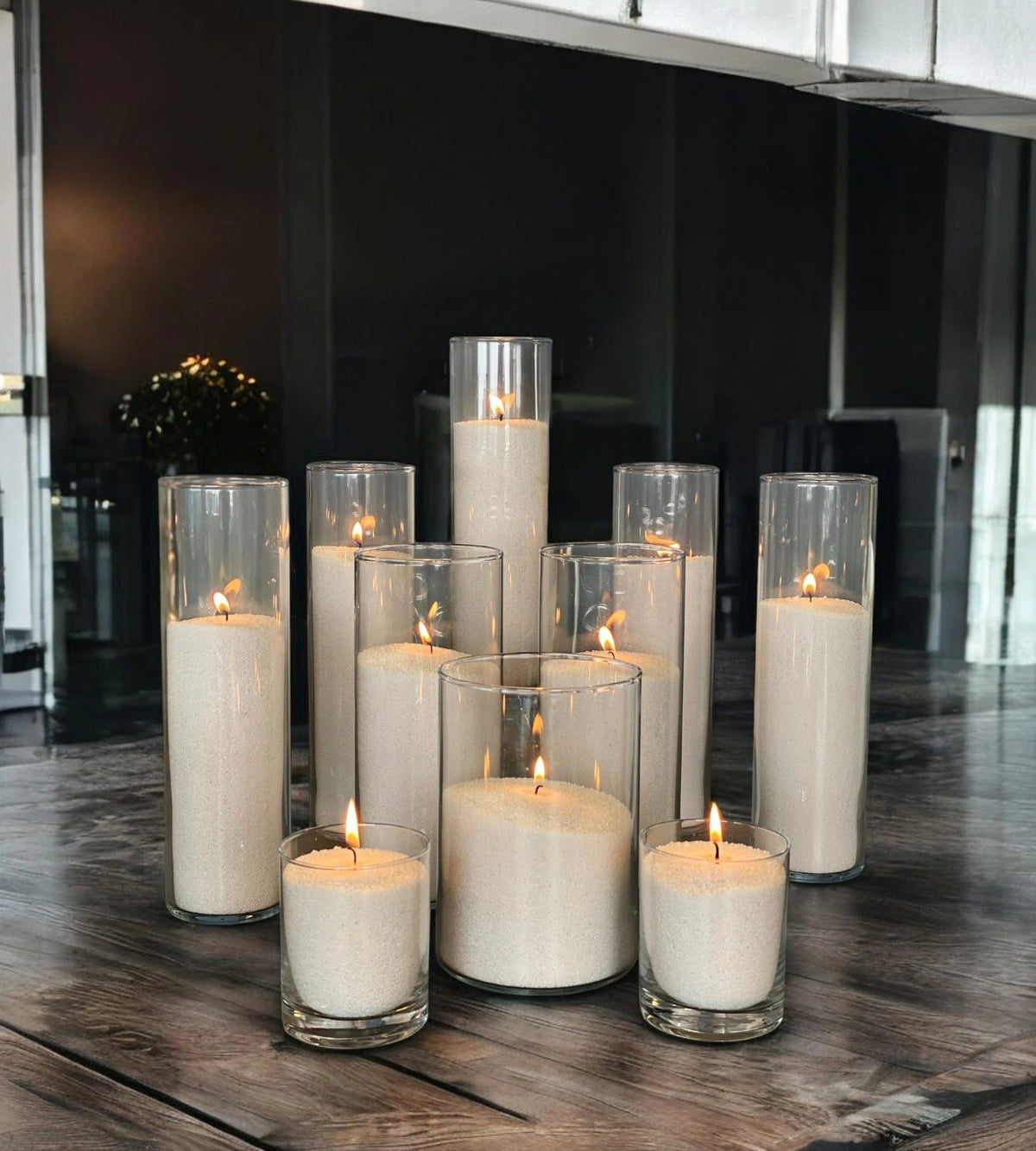 1. Multiple lit candles in glass holders arranged on wooden table in dimly lit room