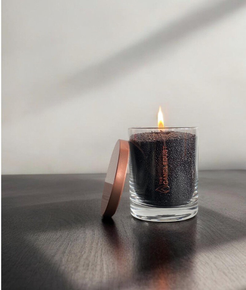 1. Single glass container with black powdered candle lit, lid beside it on dark wooden surface