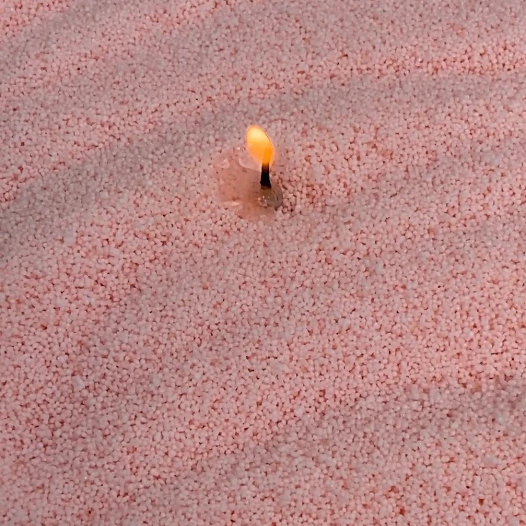 3. Close-up of lit wick in creamy peach candle sand showing texture and flame