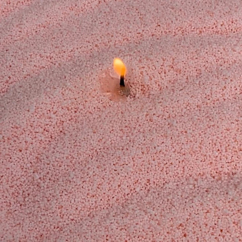 3. Close-up of lit wick in creamy peach candle sand showing texture and flame