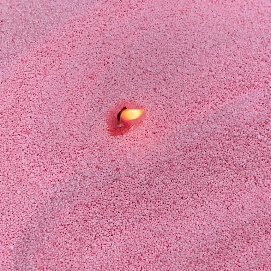 3. Close-up of lit wick in dark baby pink powdered candle wax by Candledust