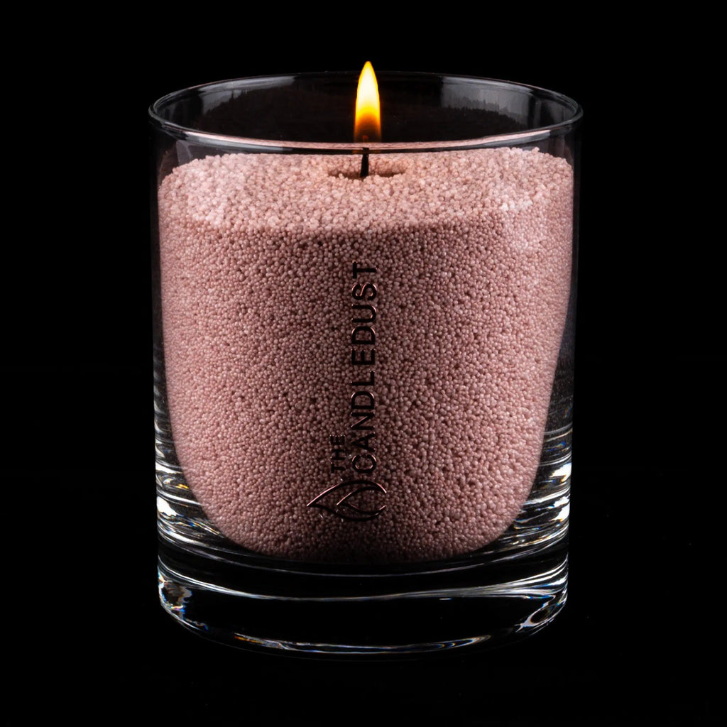 2. Glass container filled with mocha mousse colored candle sand with a lit wick, Candledust logo visible, on black background