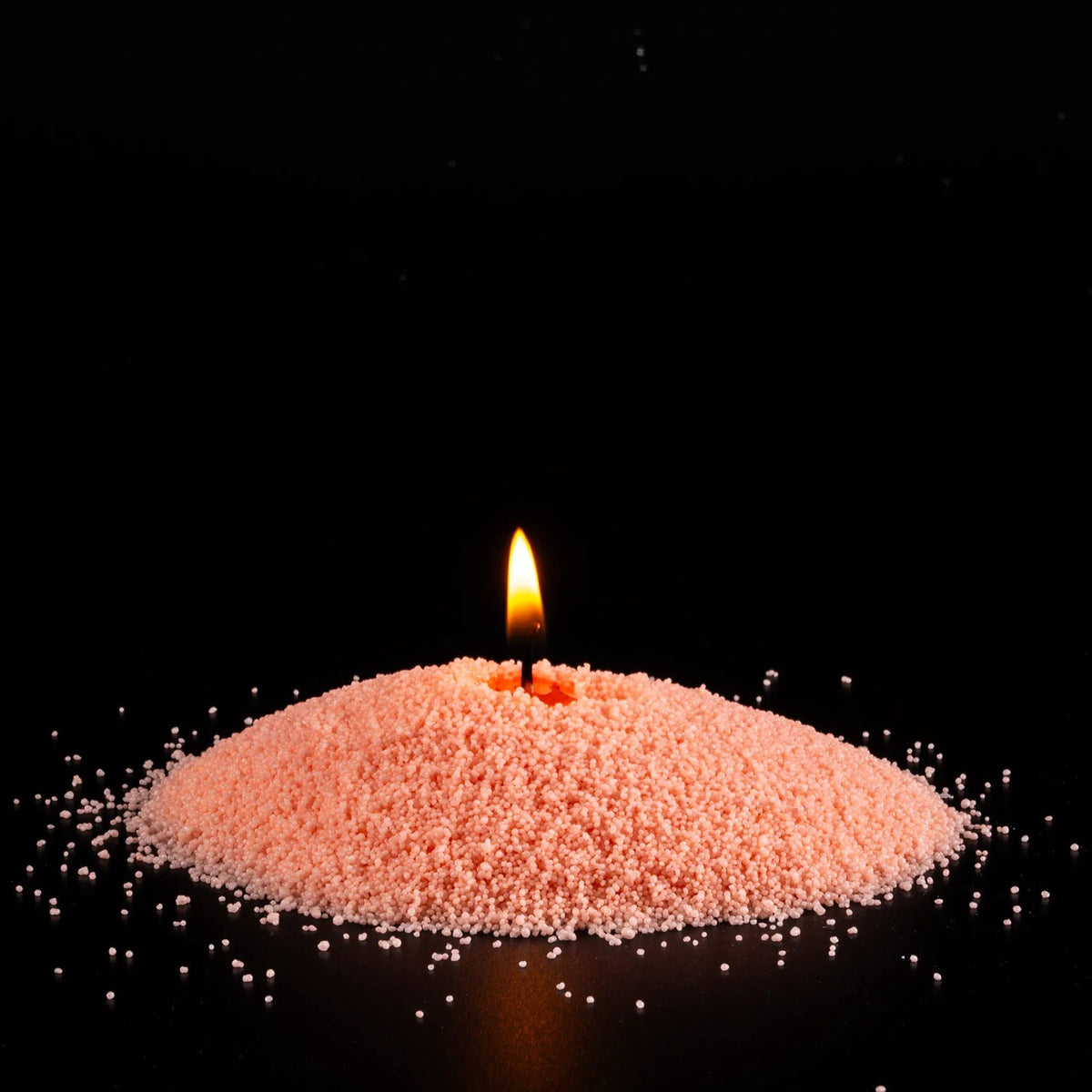 2. Unscented peach candle sand with lit wick on black background, showcasing warm glow