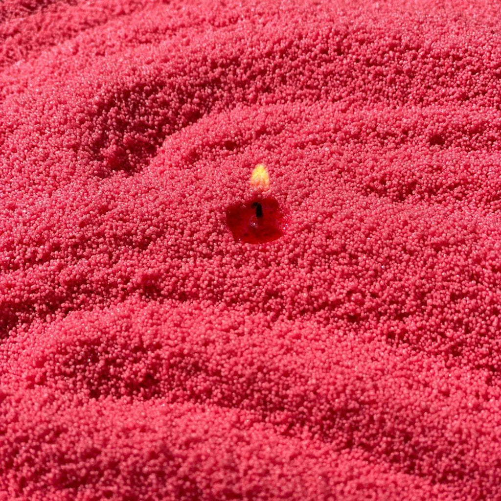 1. Close-up of lit wick in vibrant raspberry-colored candle sand, showcasing texture and color