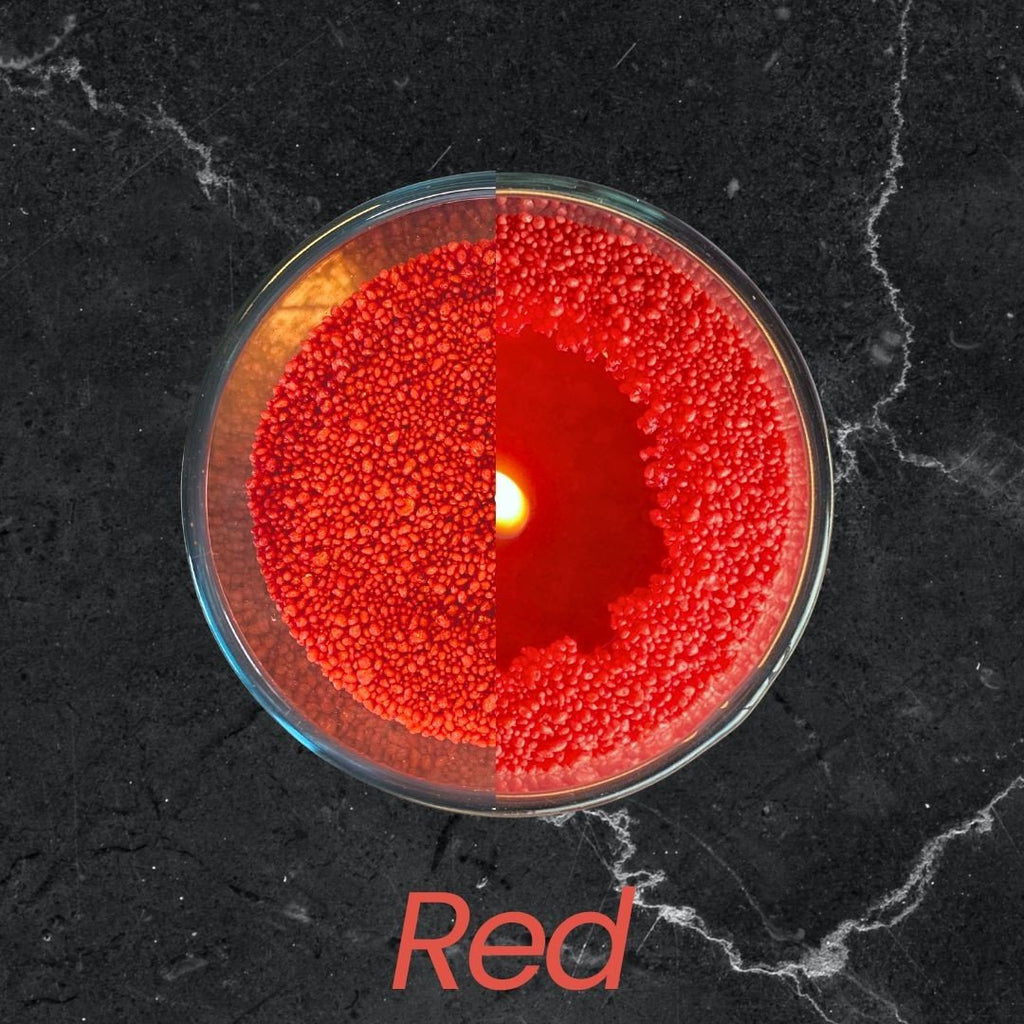3. Top view of red candle sand in glass container with lit wick on dark marble surface, text 'Red'