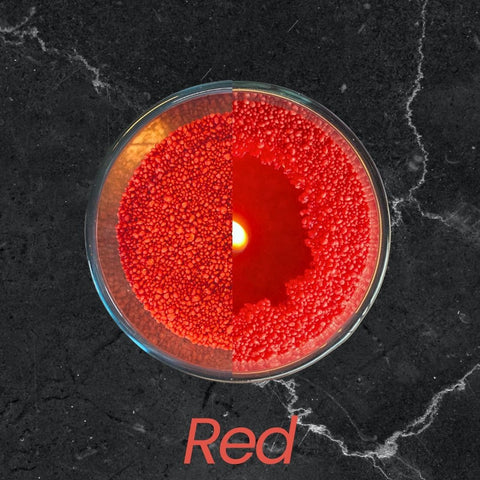 3. Top view of red candle sand in glass container with lit wick on dark marble surface, text 'Red'
